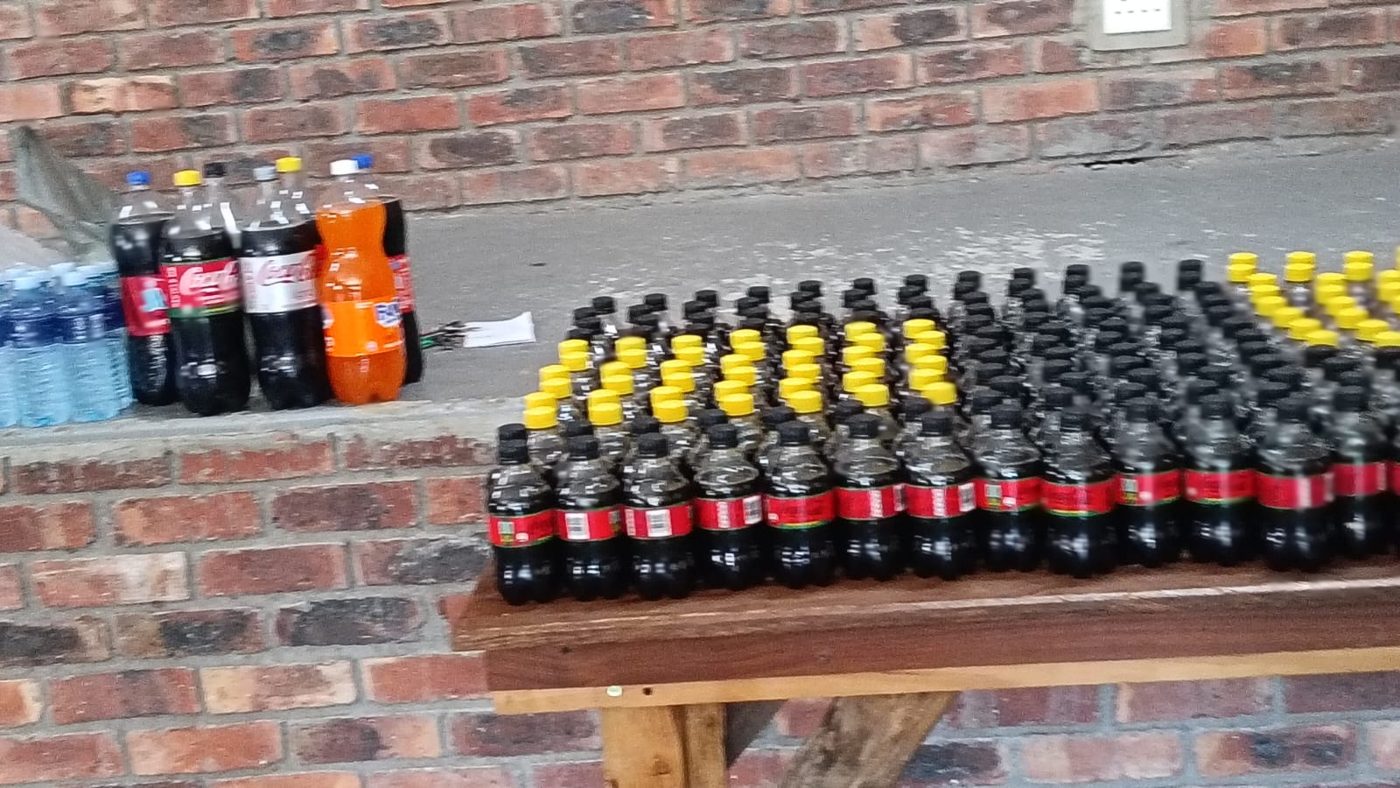 Bottles of cold drinks arranged in rows on a bench against a brick wall