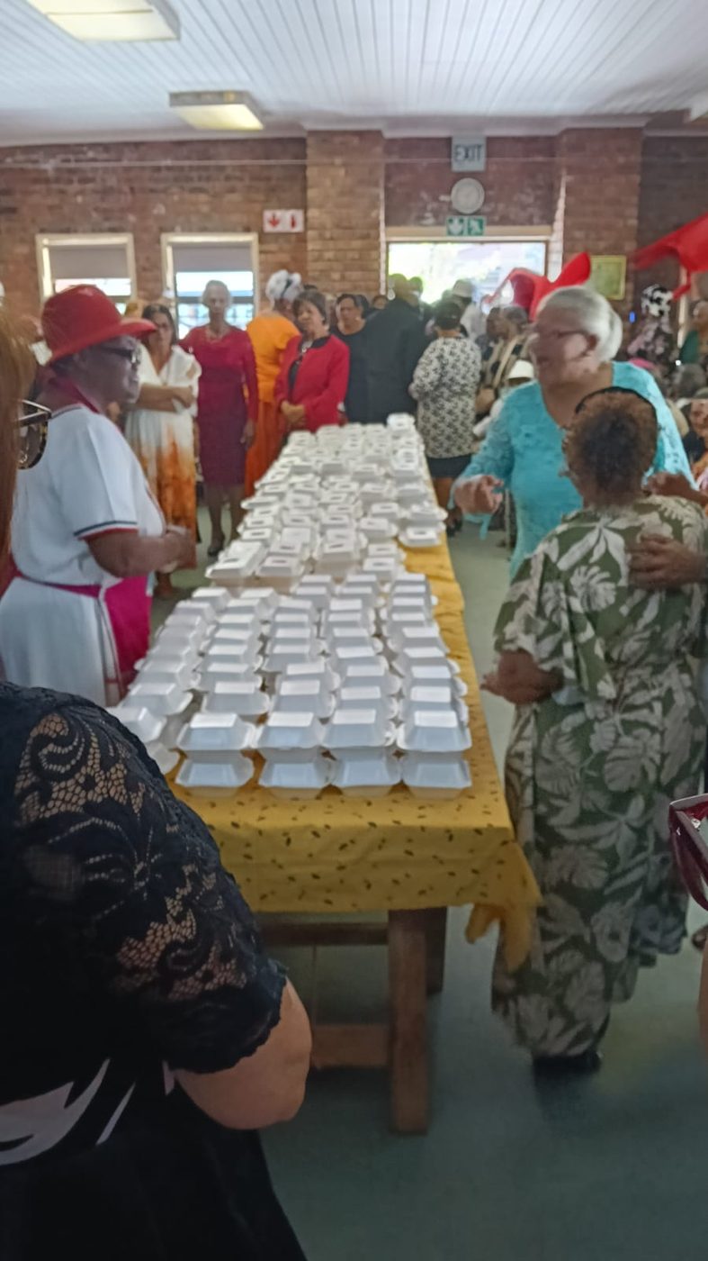 Senior citizens walking past a long table of meals laid out in rows