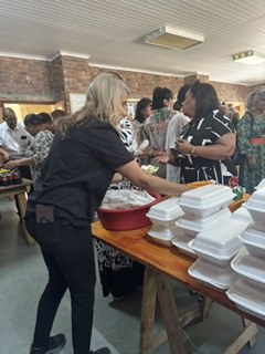 A team member arranging meal containers on a long table while guests queue behind her